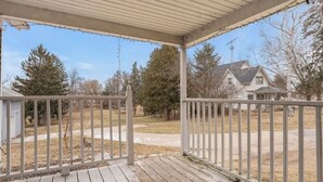 A covered porch with a view of a residential area, including houses and trees. - Pet Friendly EAA Rental (Pickett)