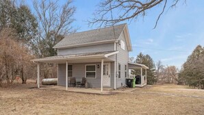 A two-story house with a covered porch, a small attached garage, and a front yard with a lawn and trees. - Pet Friendly EAA Rental (Pickett)