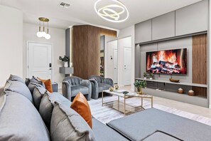 A modern living room with a grey sofa set, a coffee table, and a flat-screen TV mounted on a wooden panel wall. - 5BR house sleeps 16 with game room (Clermont)