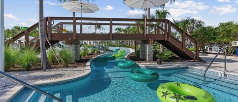 A swimming pool with clear blue water, surrounded by palm trees and a wooden bridge.