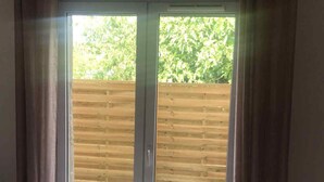 A bedroom with a bed, a sliding glass door to a balcony, and a wooden fence in the background.