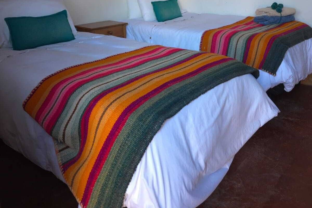 A room with two beds, each with white bedding and colorful striped blankets.