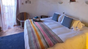 A room with a bed, a thatched roof, a window with curtains, and a small table with a chair. - Masairiatacama.cl (San Pedro de Atacama)