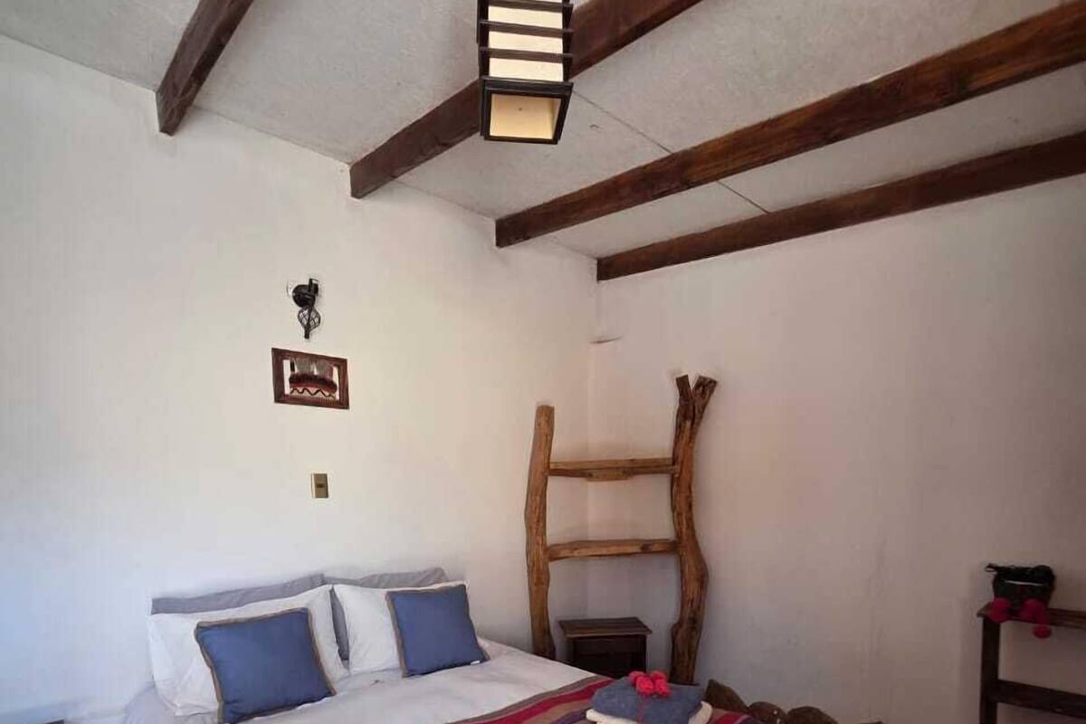 A bedroom with a bed, a wooden ladder, a wall-mounted light fixture, and a small shelf.