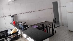 A kitchen with white tiled walls, a granite countertop, a sink, and a dining area with a table and chairs. - Complete House with Private Pool and BBQ | Praia Grande (Praia Grande)