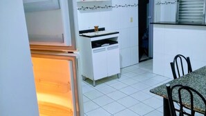 A compact kitchen with white cabinets, a built-in oven, and a dining area with a table and chairs. - Complete House with Private Pool and BBQ | Praia Grande (Praia Grande)