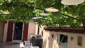 Zona salotto esterna coperta con tavolo, sedie e lampade a sospensione.