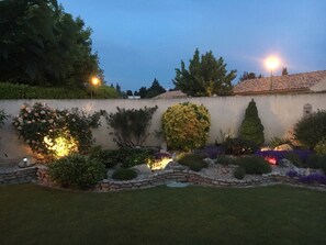 Ein gepflegter Garten mit einer Steinmauer, verschiedenen Sträuchern und einem gut beleuchteten Weg.
