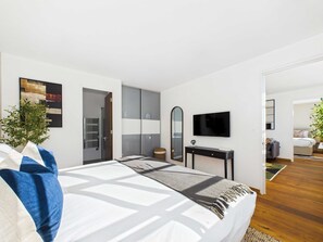A modern bedroom with a large bed, a TV, a wardrobe, and a mirror. - Bright and airy Camden Town Apartment (Greater London)