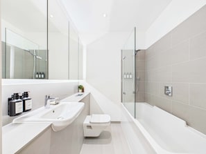 A modern bathroom with a large mirror, a sink, a toilet, and a shower area. - Bright and airy Camden Town Apartment (Greater London)