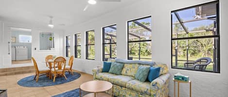 A spacious living area with a sofa, chairs, a coffee table, and a dining table. There are large windows providing views of the outdoors.