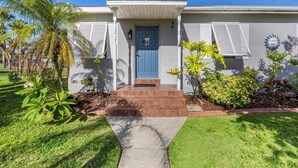 A two-story house with a blue front door, a small front porch, and a brick pathway leading to the entrance. - Right Direction Rentals Beachcomber's Retreat (Fort Pierce)