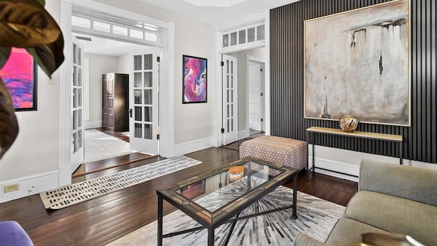 Uma sala de estar moderna com uma mesa de centro de vidro, um sofá e uma grande pintura abstrata na parede.