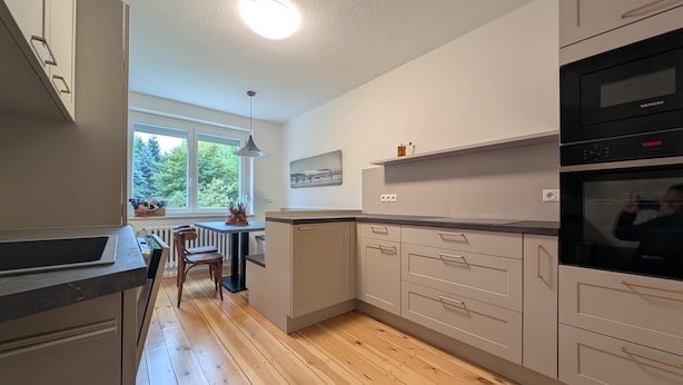 Une cuisine moderne avec des meubles gris, un plancher en bois et une fenêtre donnant sur un paysage verdoyant.