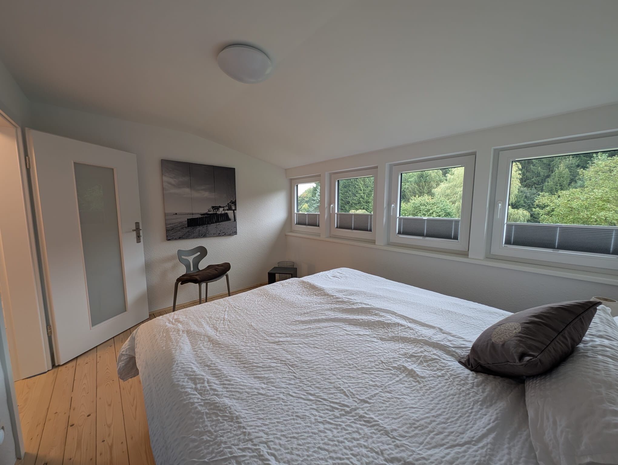 Een slaapkamer met een groot bed, een stoel, een klein tafeltje en een schilderij aan de muur.