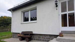 Un bâtiment à l’extérieur blanc, avec une fenêtre, un banc et un petit espace aménagé en jardin.