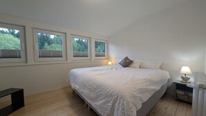 Une chambre à coucher avec un grand lit, trois fenêtres, une table de chevet avec une lampe et un radiateur.