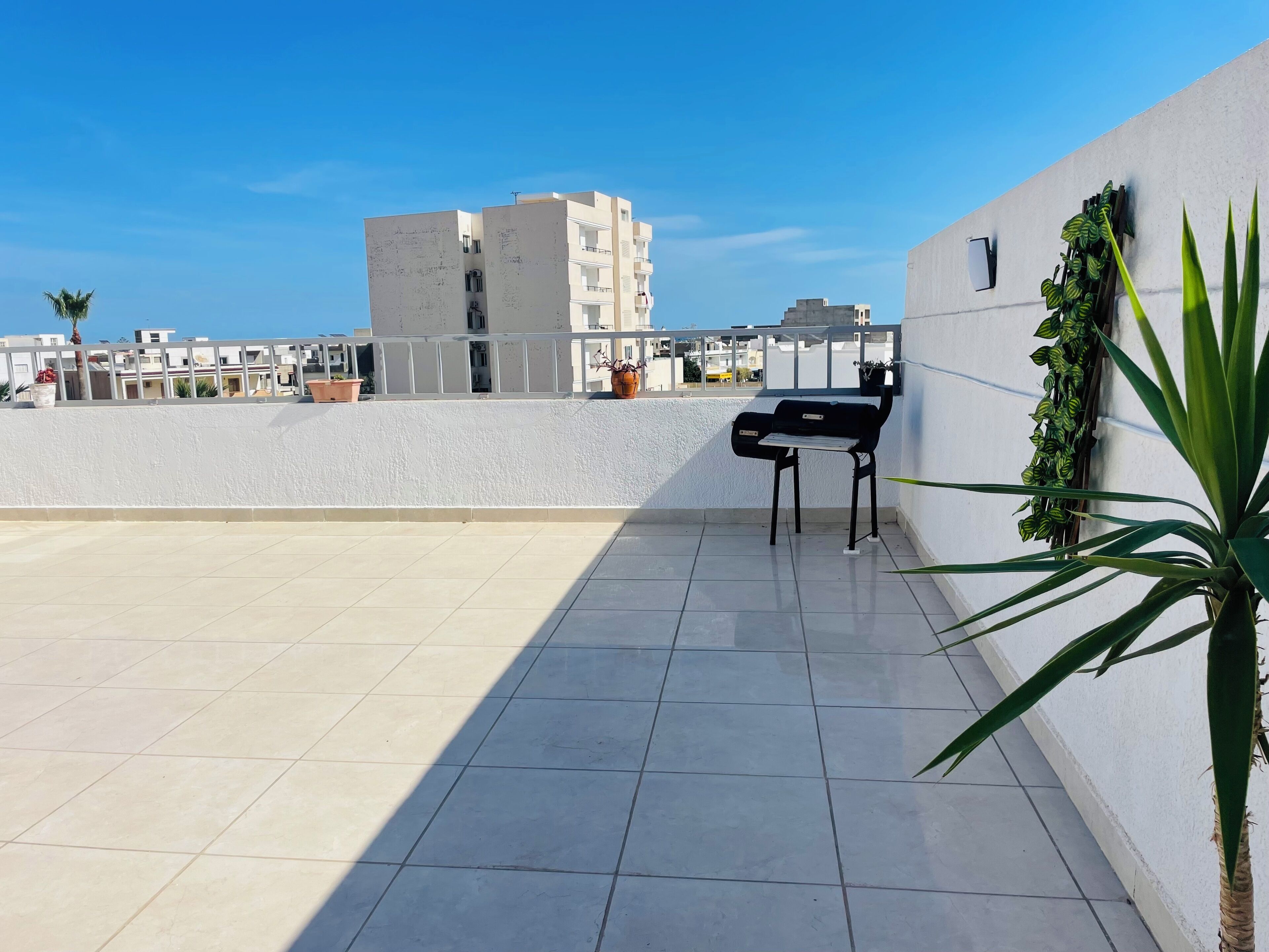 A rooftop terrace with a black chair, potted plants, and a view of surrounding buildings.