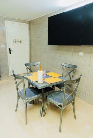 A dining area with a square table and four chairs, a white door with a coat rack, and a black cabinet above the wall. - Enjoy an unforgettable stay in this bright apartment with terrace (Mahdia)