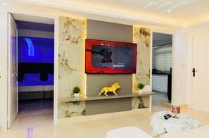 A modern living room with a flat-screen TV mounted on a marble wall, a small shelf with a lion figurine, and a cozy seating area with a white sofa and a small round table. - Enjoy an unforgettable stay in this bright apartment with terrace (Mahdia)