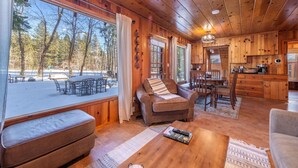 A cozy cabin interior with a dining area, a seating area with a sofa, and a view of a snowy outdoor deck. - Tahoe Golf Cabin | Walk to Beach, Hot Tub, EV & AC (Tahoe Vista)