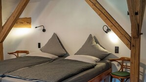 Quarto no estilo loft com teto de vigas de madeira, uma cama de solteiro, uma cadeira e uma mesinha.