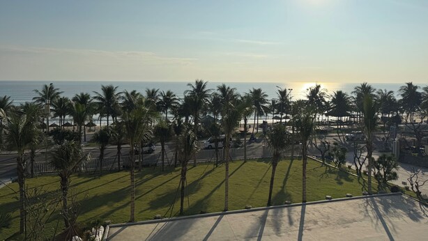 A coastal view with palm trees, a beach, and a clear sky. - My Khe Beach Hotel (Da Nang)