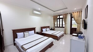A hotel room with two beds, a small desk, a refrigerator, and a window with curtains. - My Khe Beach Hotel (Da Nang)