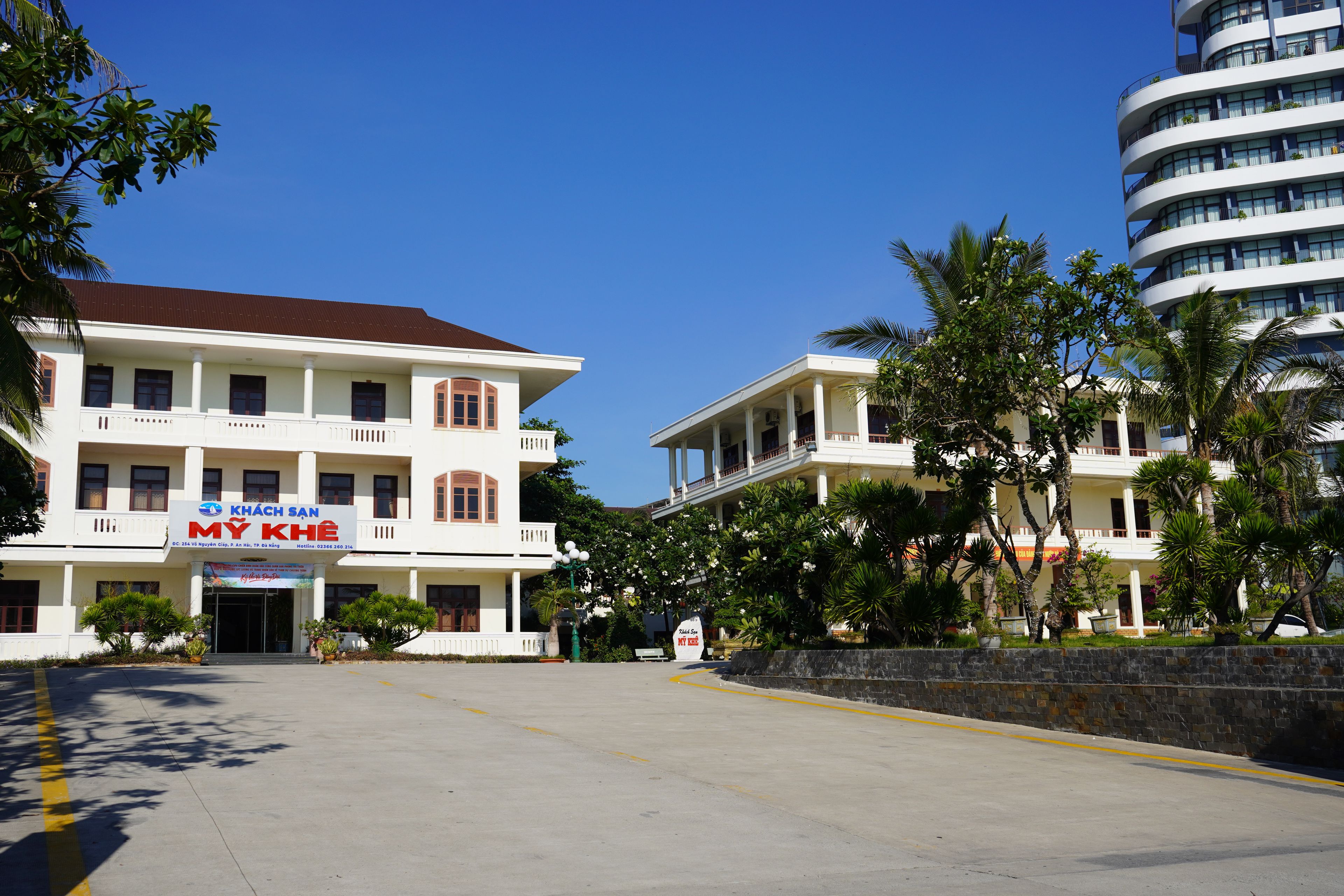 A hotel with a white facade, multiple balconies, and a clear blue sky.