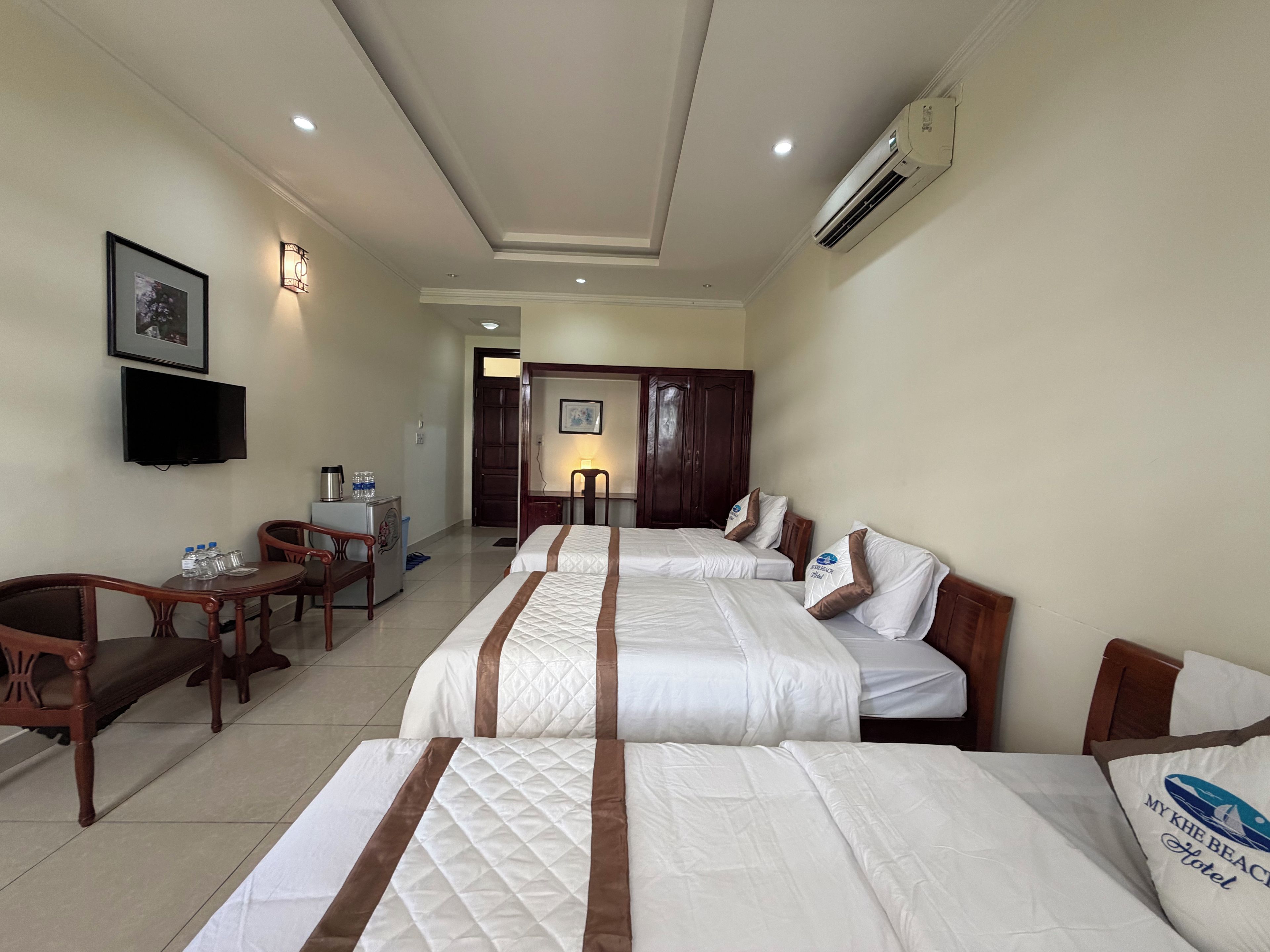 A hotel room with two beds, a desk, a chair, a television, and an air conditioning unit.
