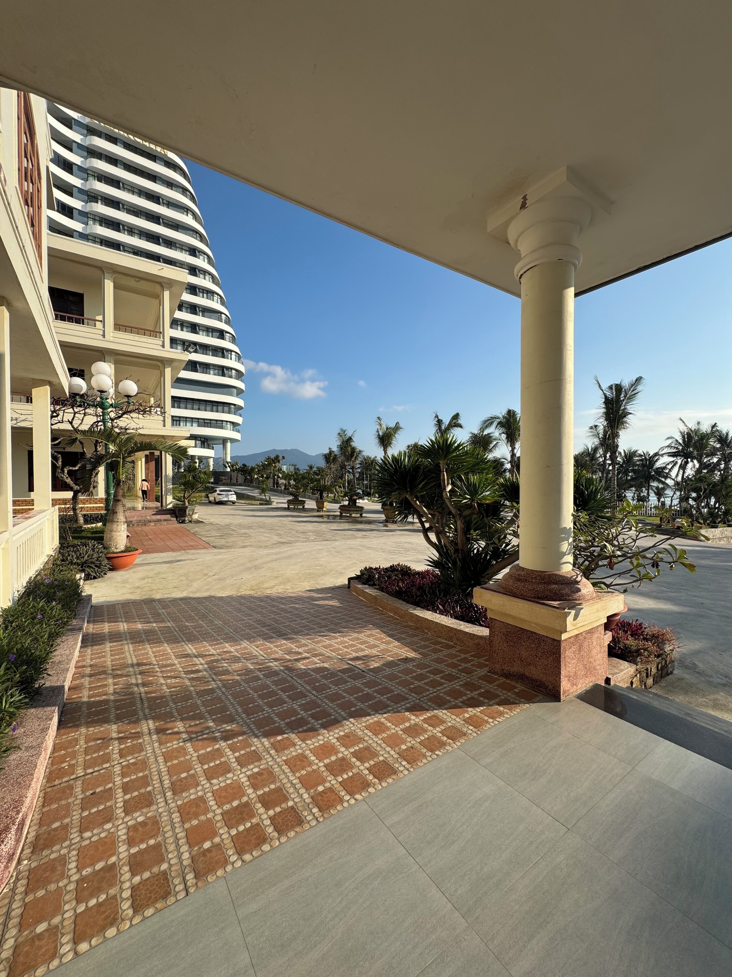 A hotel with a curved facade, outdoor seating, and palm trees.