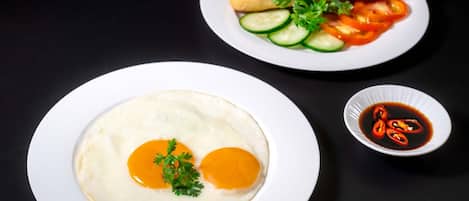 Prato com dois ovos ensolarados, decorado com salsa, um sanduíche com legumes e uma pequena tigela de molho.