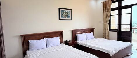 A hotel room with two beds, a ceiling light, a framed picture on the wall, and a window with curtains.