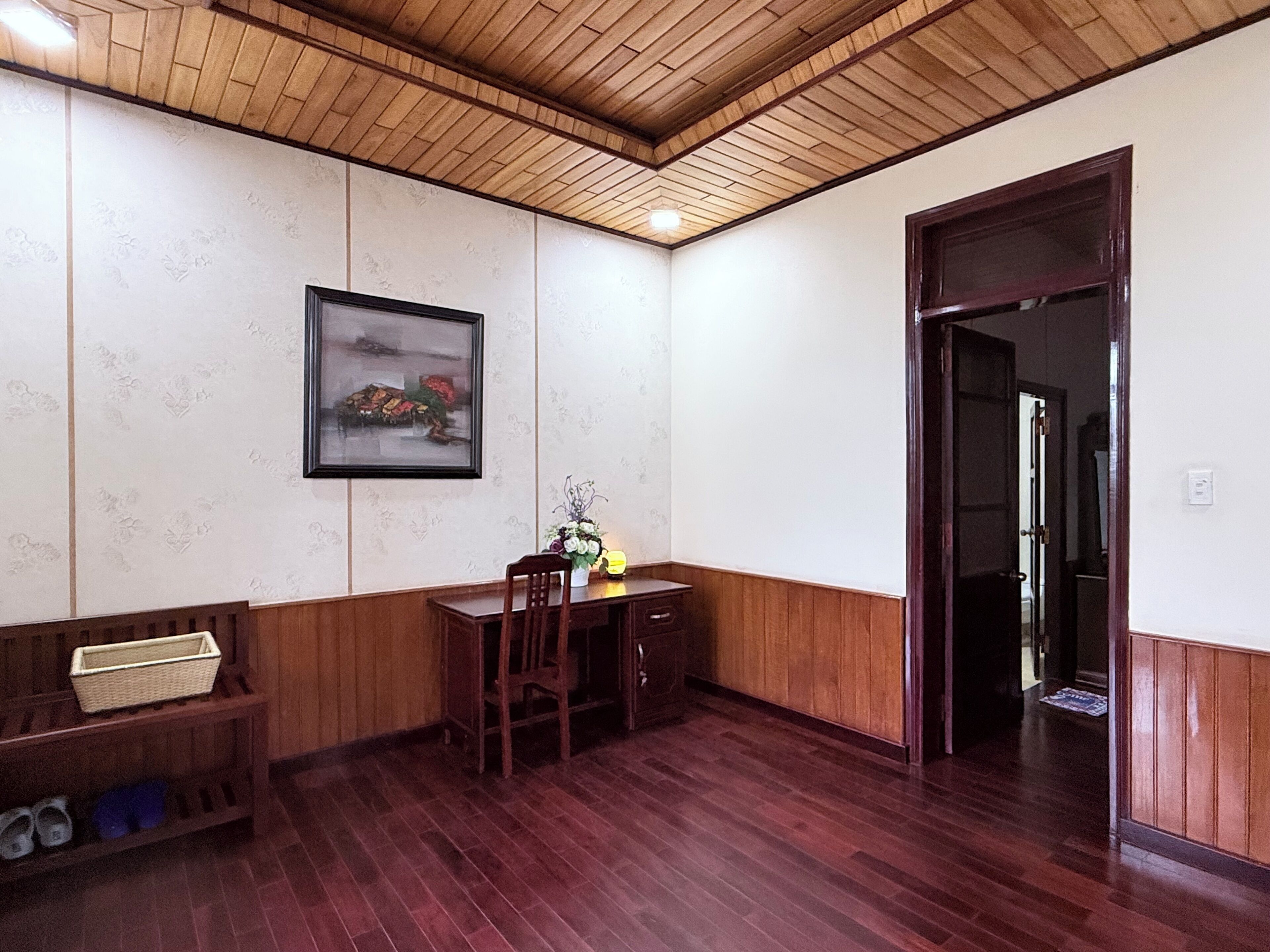 Una habitación con suelo de madera, una mesa de comedor con sillas, un banco, un cuadro enmarcado en la pared y una puerta que da a otra habitación.
