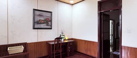 Una habitación con suelo de madera, una mesa de comedor con sillas, un banco, un cuadro enmarcado en la pared y una puerta que da a otra habitación.