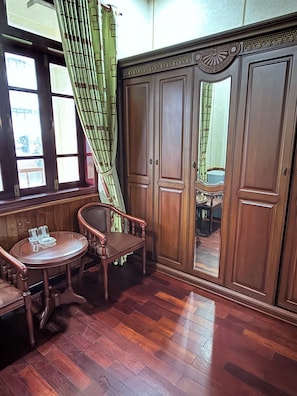 Une pièce comprenant une armoire en bois, une chaise, une petite table ronde avec des salières et des poivrières, et une fenêtre avec un rideau vert.