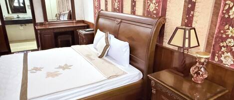 A neatly made bed with a floral bedspread, a wooden nightstand with a lamp, and a mirror on the wall.
