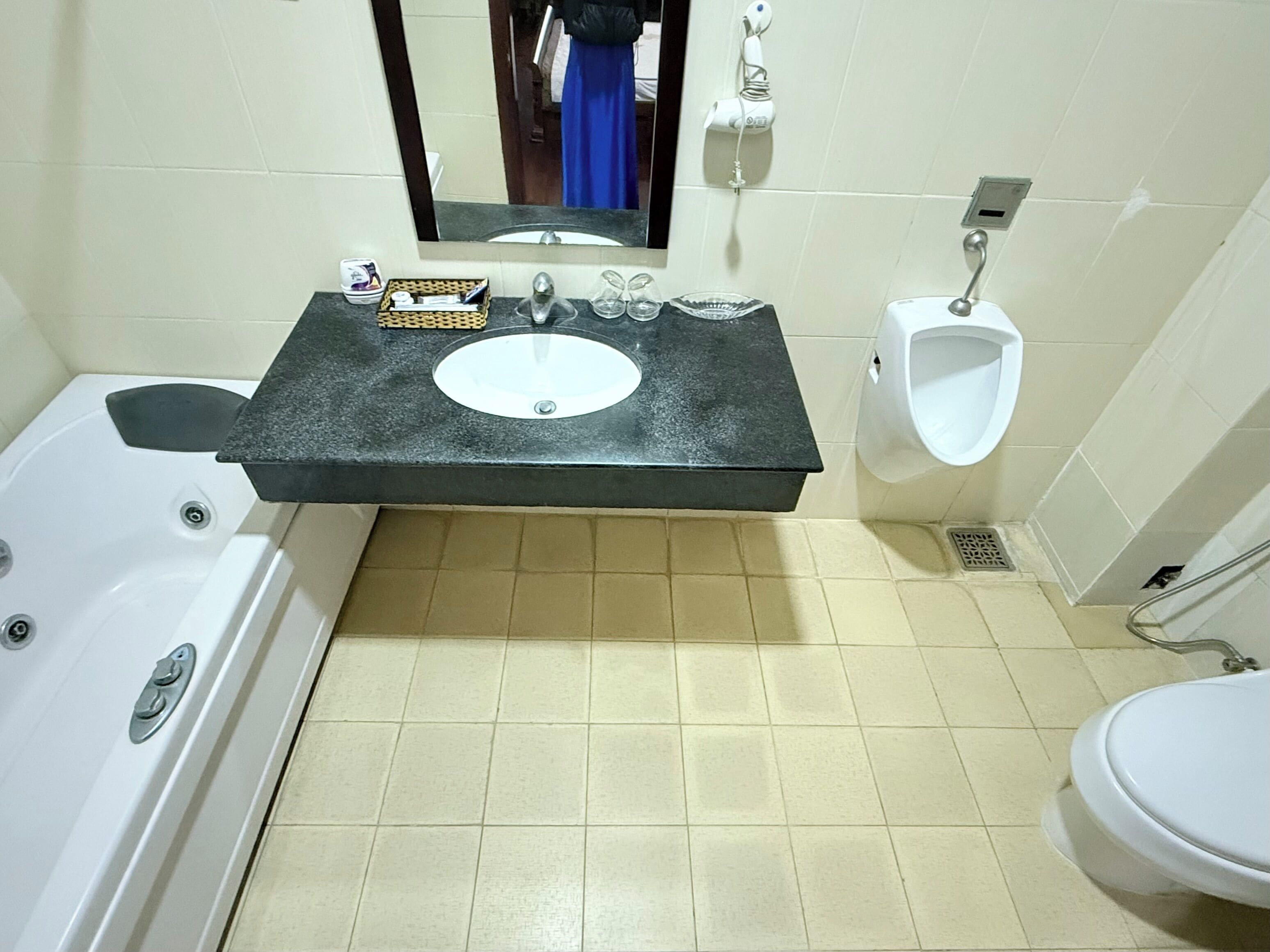 Ein Badezimmer mit Badewanne, Waschbecken mit Spiegel, Urinal und Toilette.