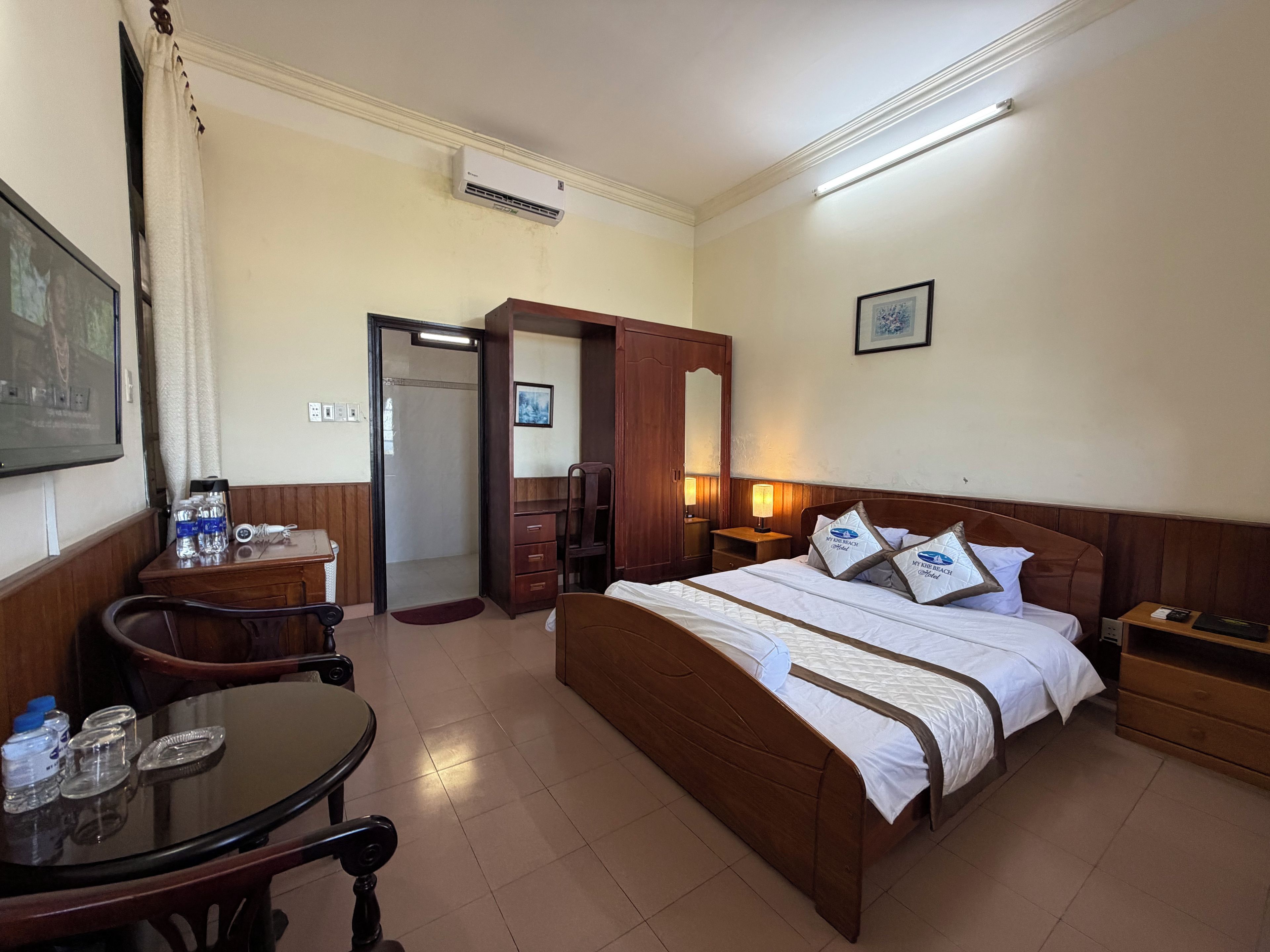 A hotel room with a bed, bedside table, desk, chair, and a television.