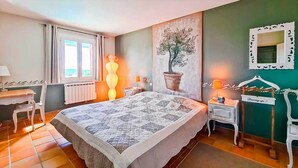 A bedroom with a large bed, a window with curtains, a potted plant, a dresser, and a mirror. - Charming family home with heated pool in the Gard (Méjannes Lès Alès)