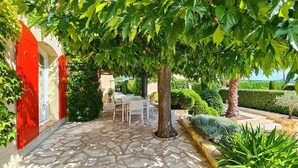 A stone-paved courtyard with a red door, a table and chairs, and various plants. - Charming family home with heated pool in the Gard (Méjannes Lès Alès)