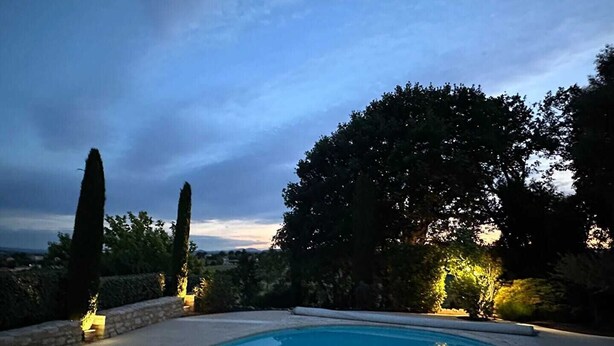 A swimming pool with a curved edge, surrounded by a stone wall and tall trees. - Charming family home with heated pool in the Gard (Méjannes Lès Alès)
