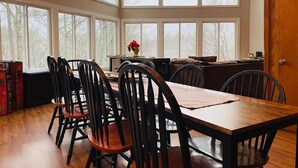A dining area with a wooden table and chairs, large windows, and a view of trees. - Mountain View, Dogs OK, 2 Kitchens, Screened Deck, Pool Table, North Conway (Conway)