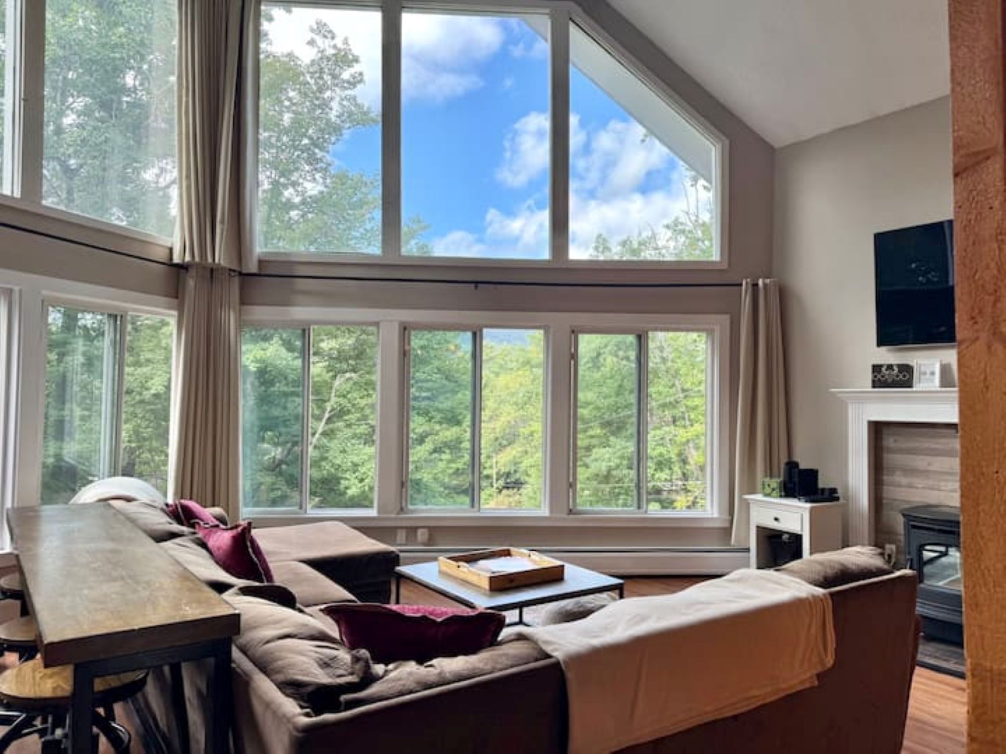Una habitación amplia con un gran ventanal, un sofá, una mesa y una chimenea.
