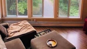 A room with large windows offering a view of a forested area. There is a sofa and a small table with a bowl on it. - Mountain View, Dogs OK, 2 Kitchens, Screened Deck, Pool Table, North Conway (Conway)