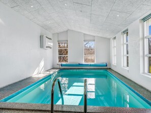 Una piscina interior con agua azul cristalina, suelo de baldosas y un banco a lo largo de la pared.