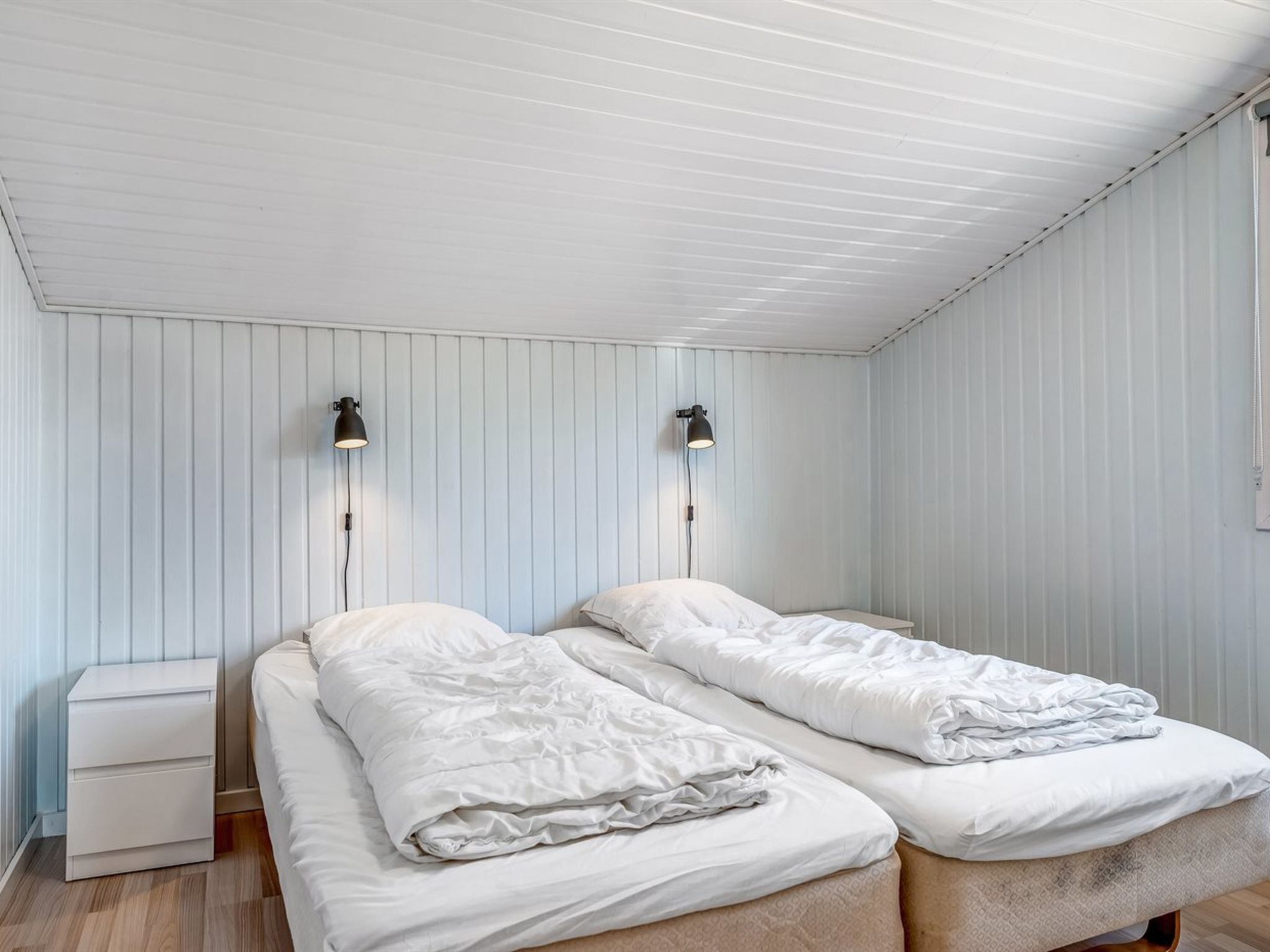 Una habitación con dos camas, una mesita de noche y dos lámparas de pared.