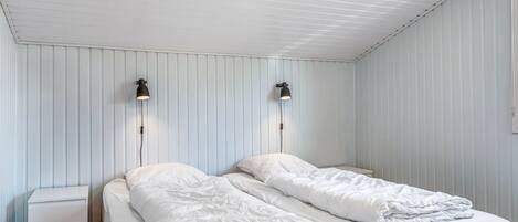 Una habitación con dos camas, una mesita de noche y dos lámparas de pared.
