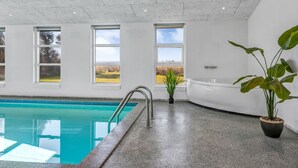 Une piscine intérieure moderne offrant une vue dégagée sur l’extérieur grâce à de grandes fenêtres.