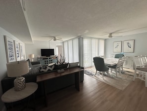 A modern living room with a flat-screen TV, a dining area with white chairs, and artwork on the walls. - Waterfront 2 bed/2 bath condo on Boca Ciega Bay on highly desirable Isla del Sol (St. Petersburg)